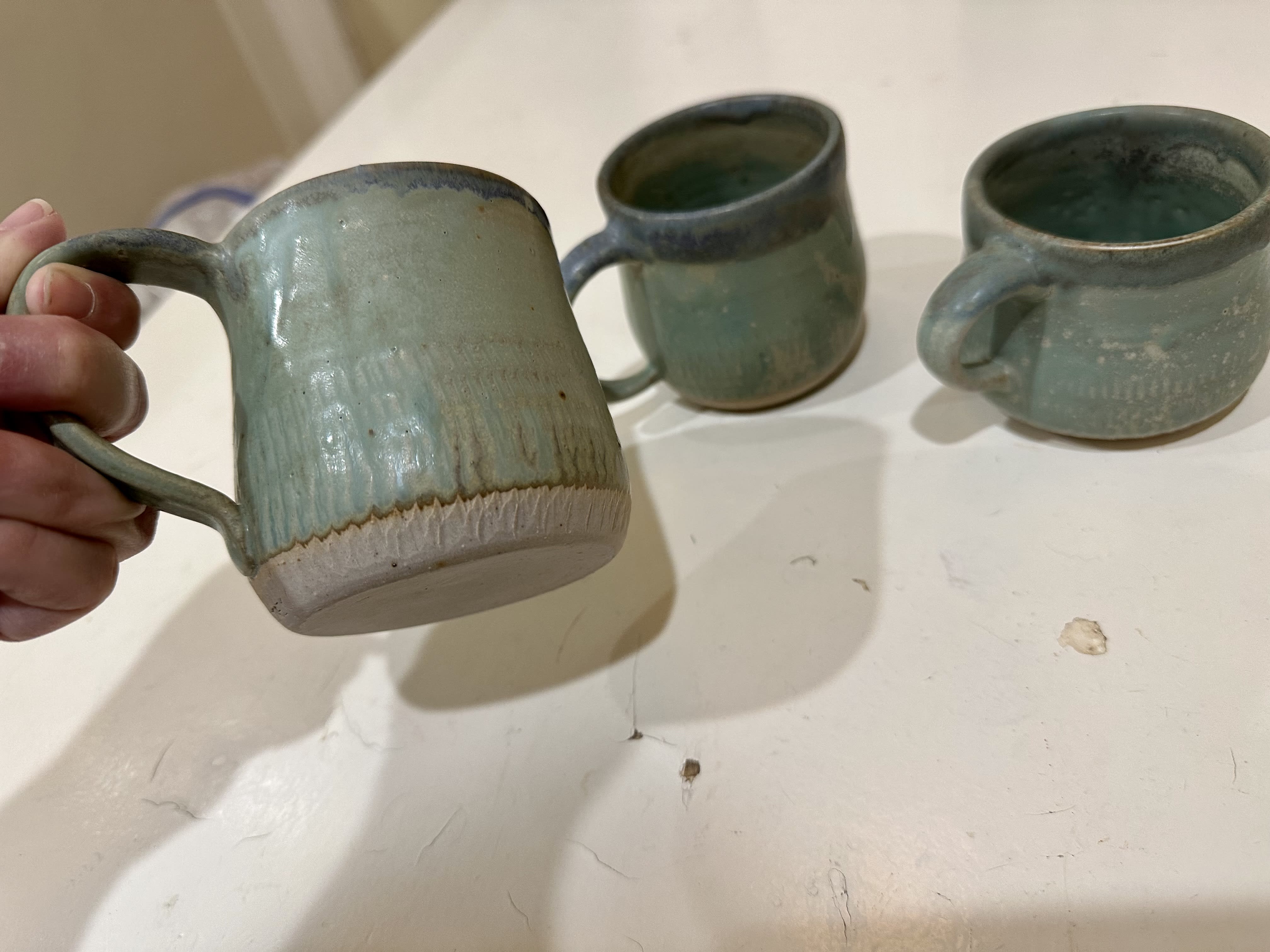 Three turquoise mugs, one being held