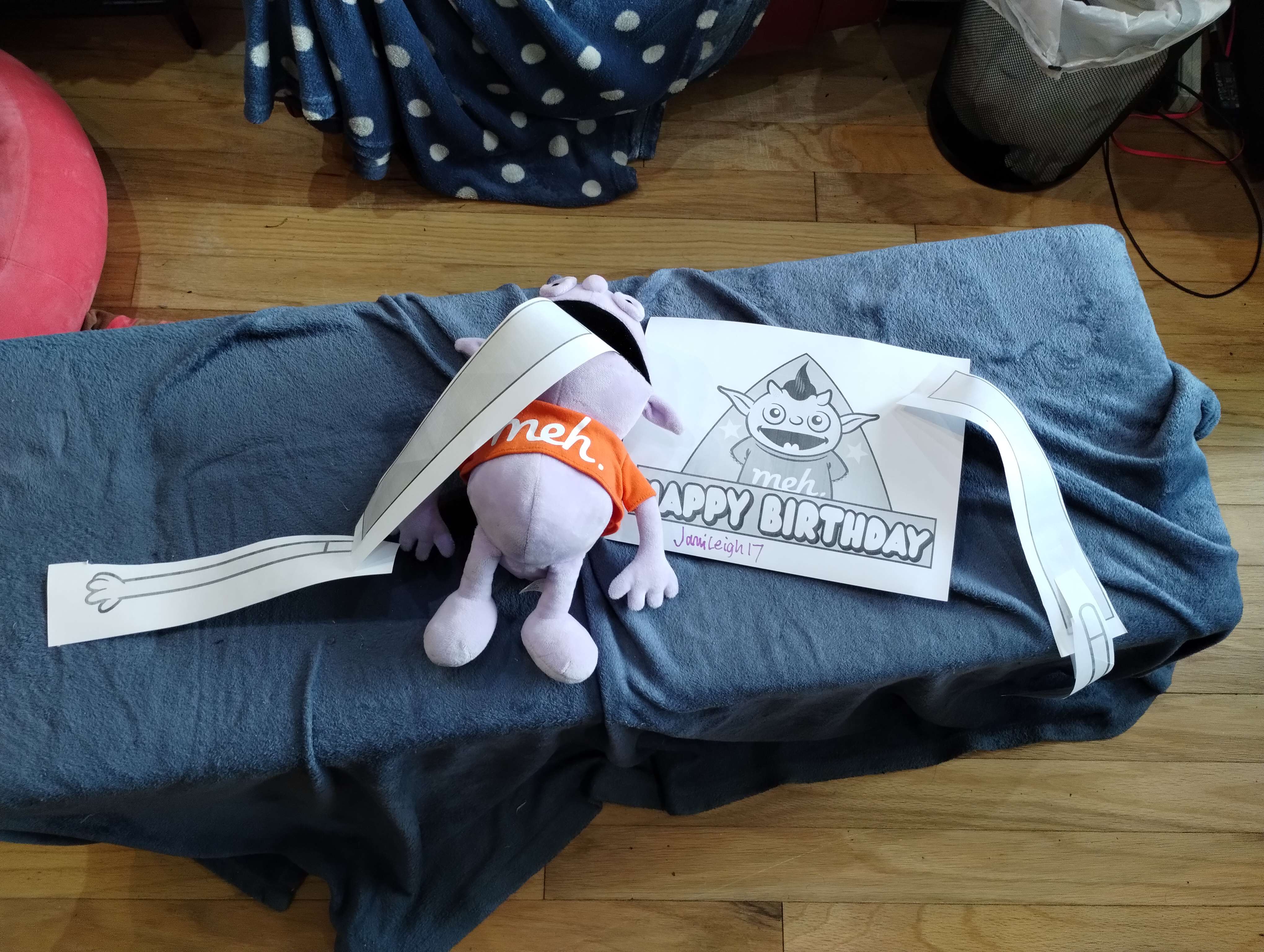 birthday hat image with one arm on the paper, the other arm hanging out of the mouth of an Irk stuffy