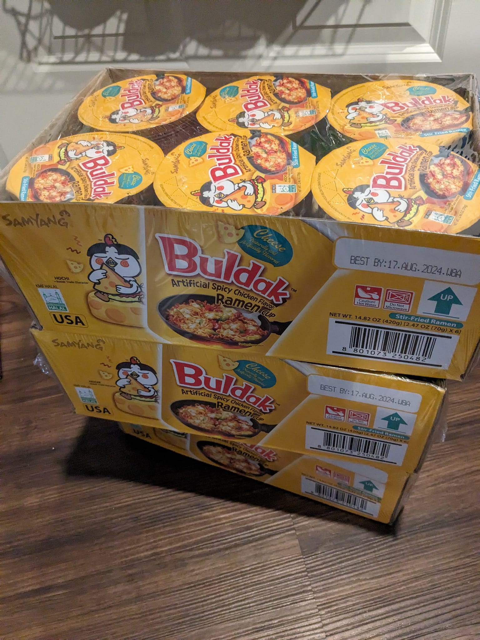 3 boxes of Cheese Buldak stacked on the floor in front of a pantry
