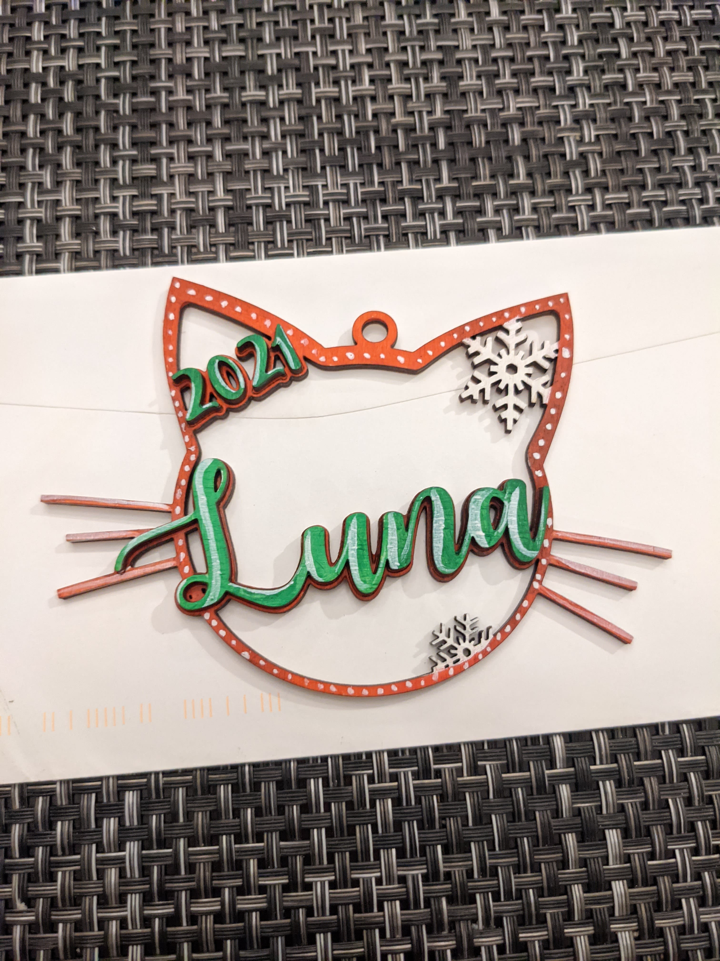 Wooden cat-shaped ornament painted red and green that says Luna across it and 2021