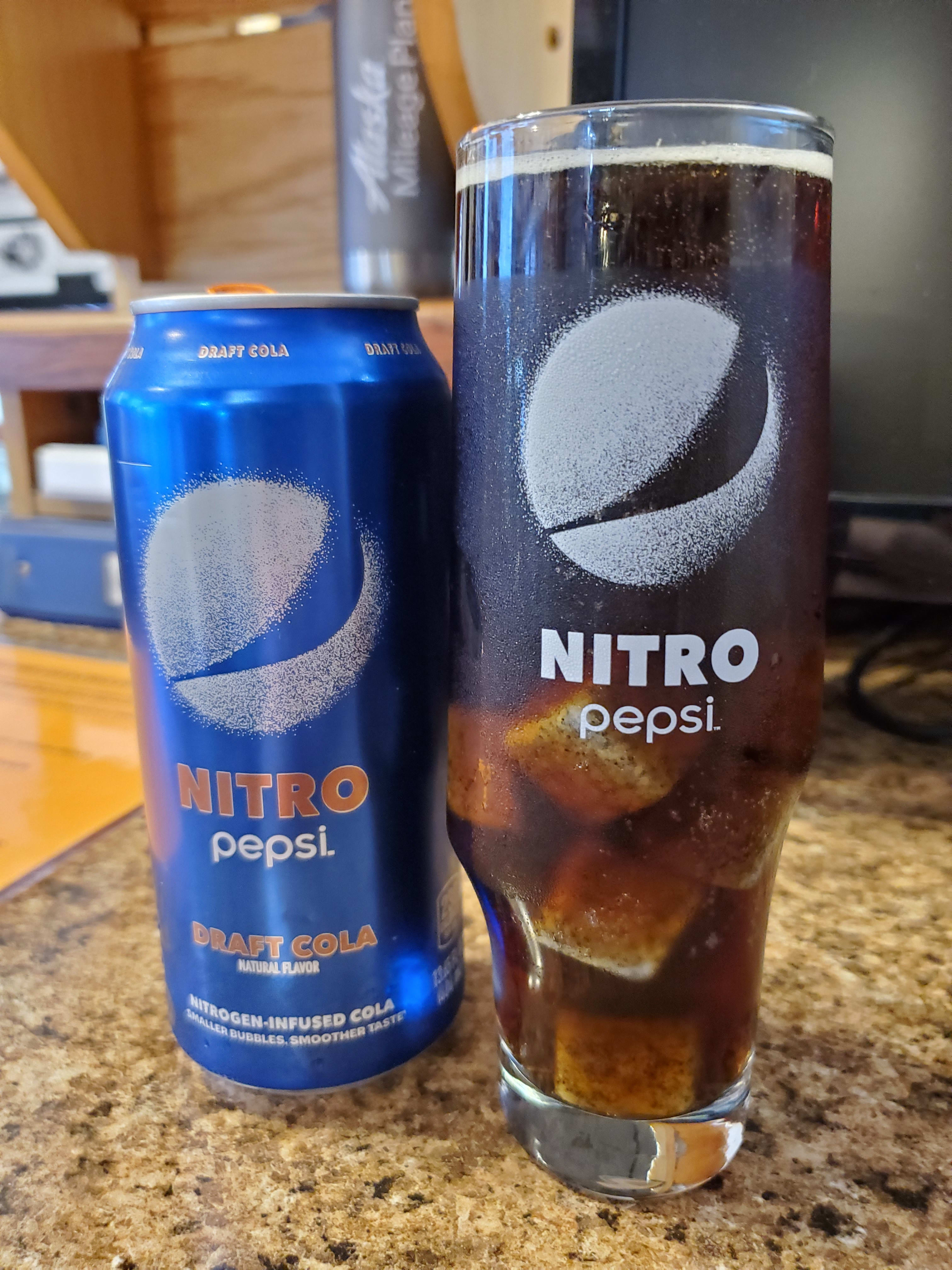 A can of Nitro Pepsi with the matching glass filled with the eponymous soda, and some whiskey stones.