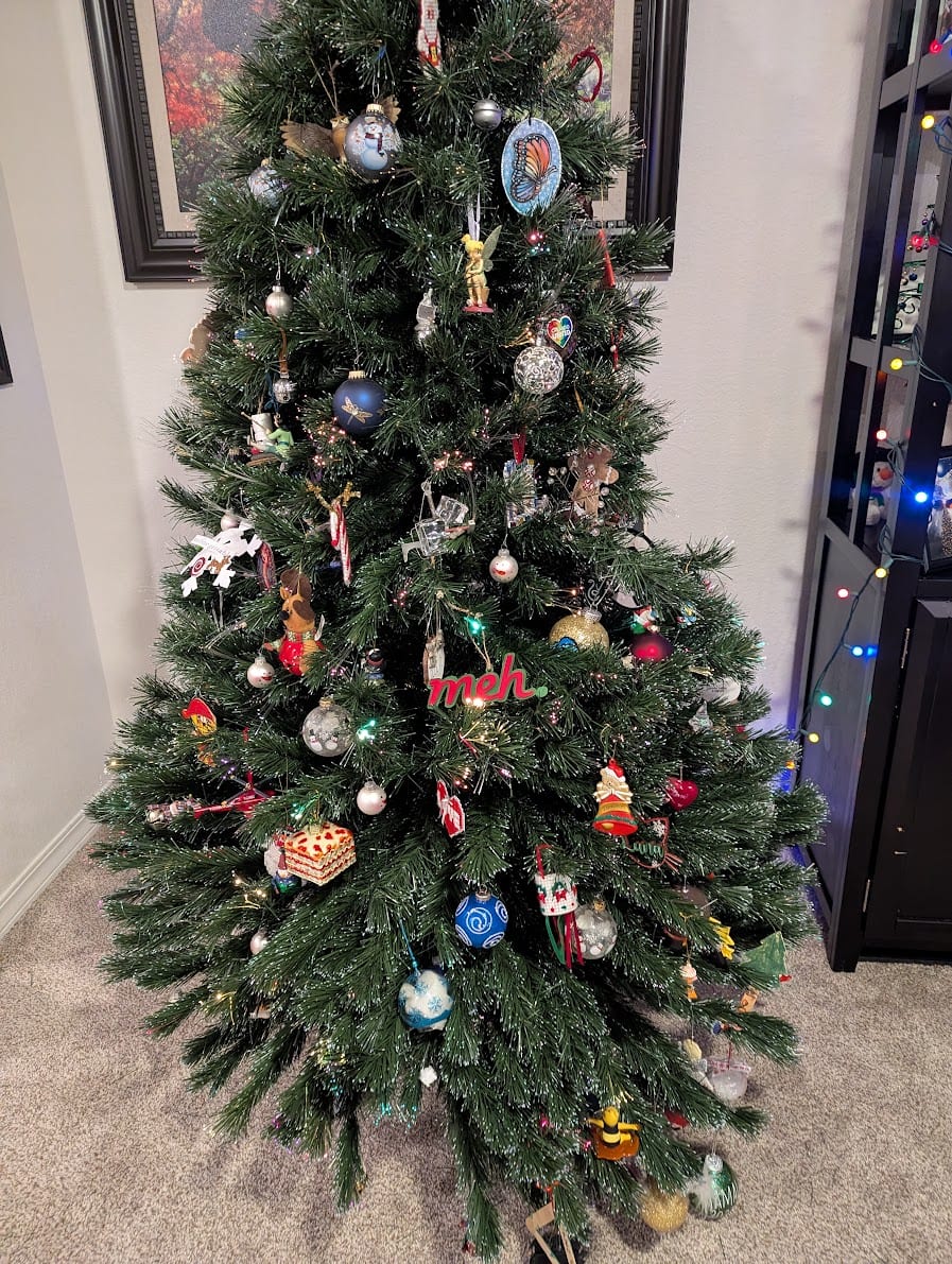 A Christmas tree decorated with many ornaments, including a "meh." ornament front and center.