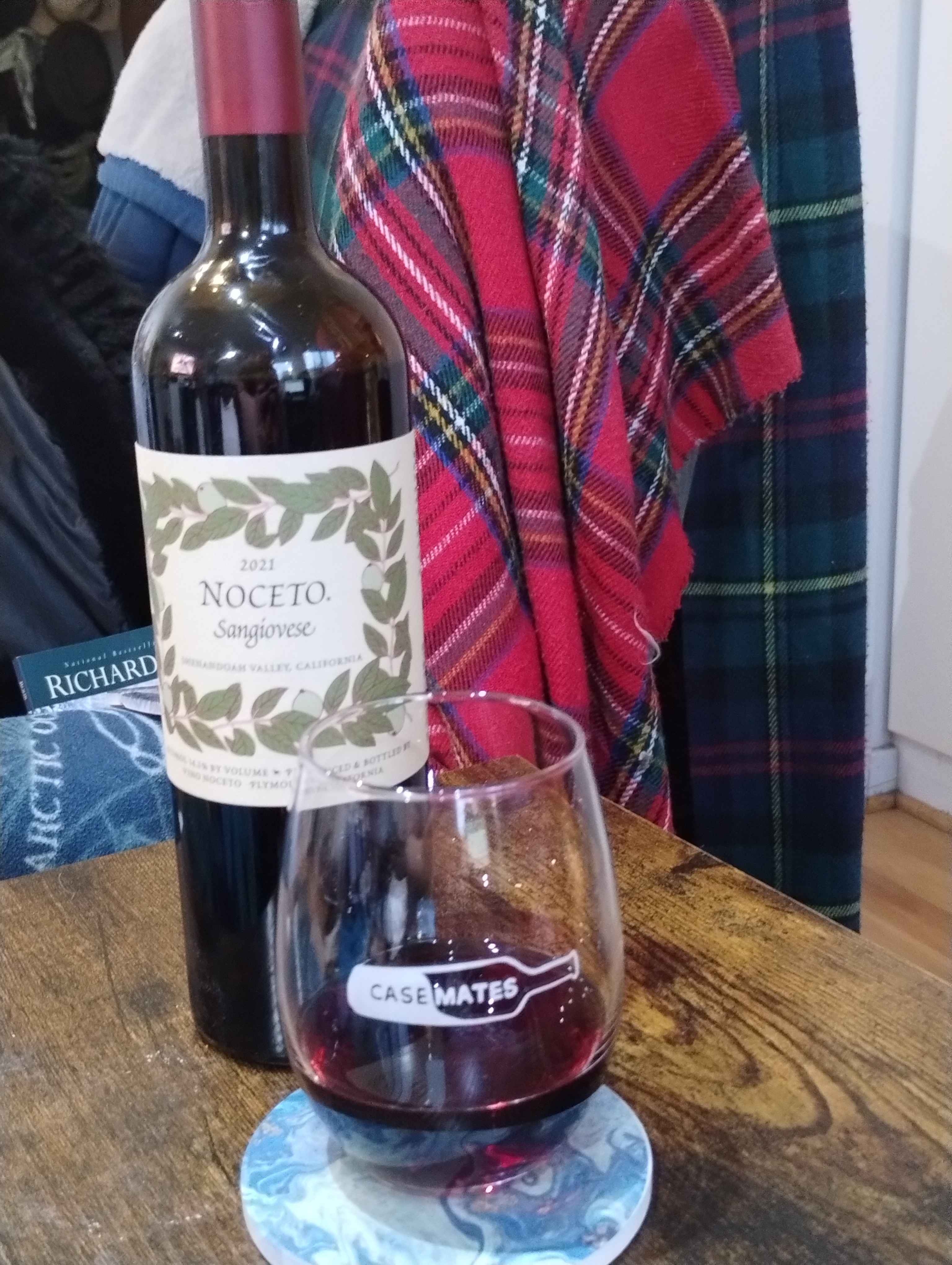 Red wine in a casemates glass on a blue coaster, on a dark wood table, with the bottle in the background